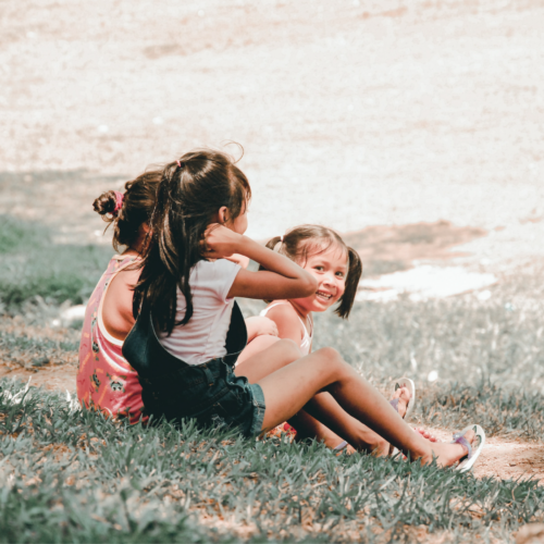 Three happy kids sit on a grassy hill. Explore Britt Hawthorne’s recommendations for children’s books on love. Photo: Charlein Gracia