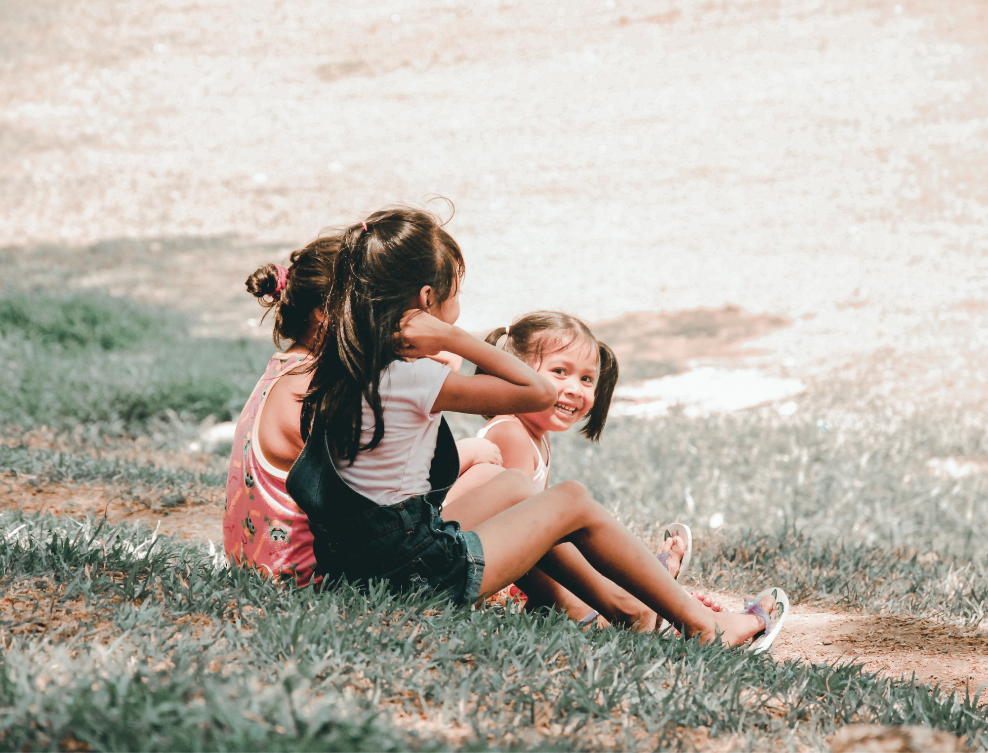 Three happy kids sit on a grassy hill. Explore Britt Hawthorne’s recommendations for children’s books on love. Photo: Charlein Gracia