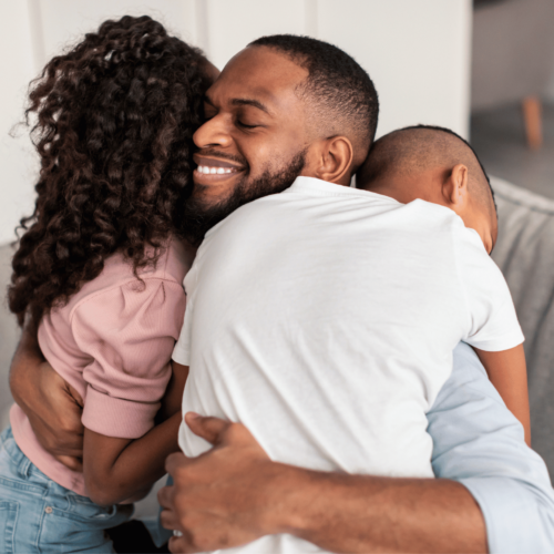 Black man sits on a couch and hugs two children. Explore books about consent for every age with Britt Hawthorne